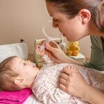 Mother cleaning mucus of baby with nasal aspirator